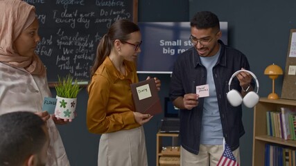 During interactive English lesson, teacher and diverse students labelling everyday objects like flower, diary, and headphones with sticky notes to practice vocabulary - Powered by Adobe