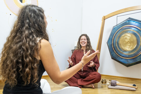 female teacher guiding a sound healing session with a student in a meditation space, with a large octagonal gong and Tibetan singing bowls on the floor, concept of spiritual music and energy therapy