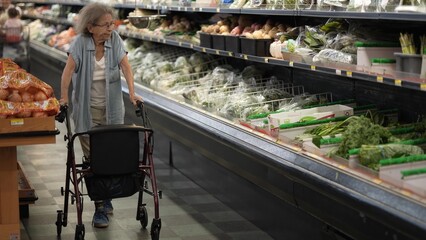 A disabled elderly woman navigates the grocery store using her walker while selecting fresh...