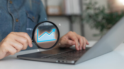 A woman analyzing a financial growth chart on a laptop with a magnifying glass, concept of business...