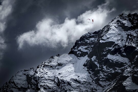 Two paragliders over snowy peak with dramatic clouds, Sellrain, Innsbruck, Tyrol, Austria