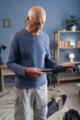 An old man preparing for a hike checks the completeness of the tent holds the parts for assembly in...