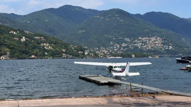 Como, Italy, A swinging Cessna 172 &ldquo;Skyhawk&rdquo; Seaplane, is moored to the pier at Lake Come Seaplane base, front of wooded and partly built-up mountain landscape at Lake Como - 4k video footage