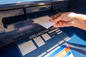 Close up of a woman's hand as she drops letters into the slot on a mail collection box 