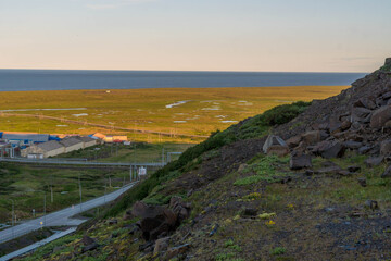 Bering Sea coast extends across Chukotka Peninsula, Russia, with grassy tundra dotted by ponds and a winding road near the remote Arctic border with Alaska.
