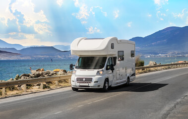 Camper van drives along a road along the seashore with mountains
