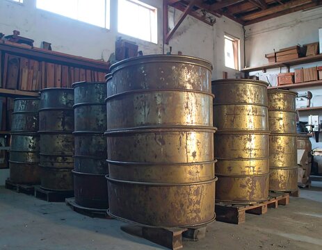 Stacks of large tarnished metal barrels in an industrial storage space with wooden shelves