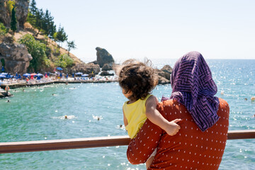 Woman is holding a child on a pier by the ocean