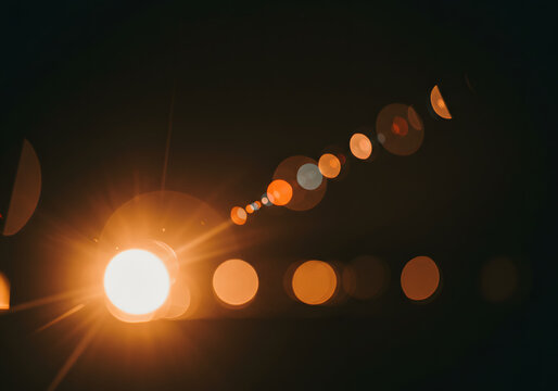 Bright light source with lens flare, creating a trail of bokeh circles against a dark background.