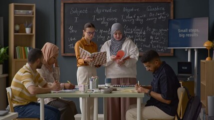 Multicultural group of students engaging with their teacher during interactive English language lesson in modern classroom setting with chalkboard and table