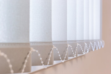 Close-up of vertical fabric blinds with bead chain connectors, offering light control and privacy...