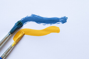 Two strokes of blue and yellow paint applied with brushes on a white sheet of paper, symbolizing...