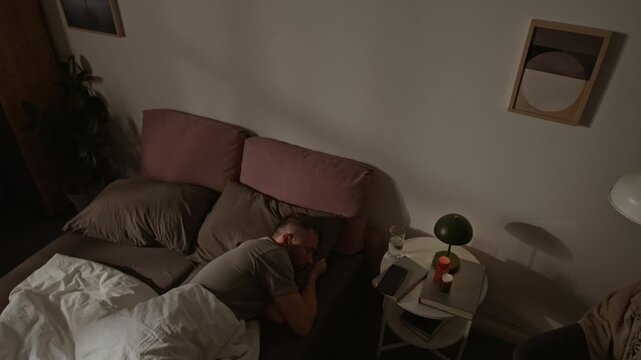 Time lapse of young Caucasian man sleeping in bed at night in darkness until morning, tossing and turning, hugging pillow, lying on back, side, face down, shadows shifting on bedroom wall