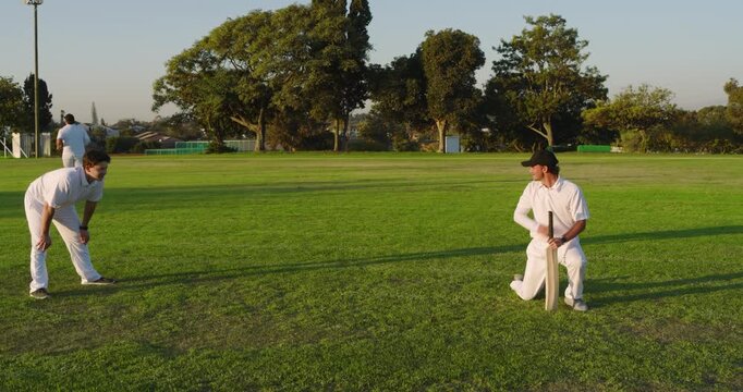 Bowler delivering red ball triggers male cricket team practicing sweep shots on pitch, copy space