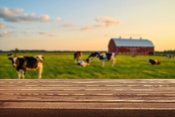 Wooden table, cows grazing in a scenic countryside farm during golden hour with a barn in the...