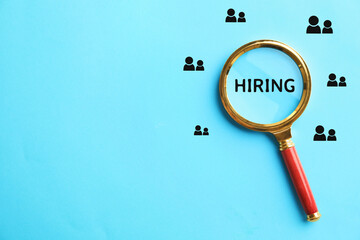 Word Hiring and human icons on light blue background, view through magnifying glass