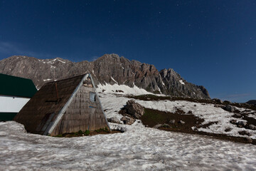 Mountain landscape with wooden cabin under a starry night sky in winter setting on a snowy terrain