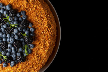 Delicious cake topped with fresh blackberries and blueberries on a dark background