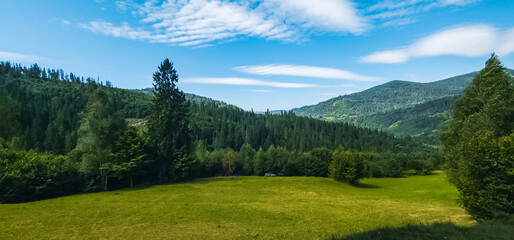 A stunning mountain landscape with lush greenery under a vibrant blue sky with wispy clouds, ideal...