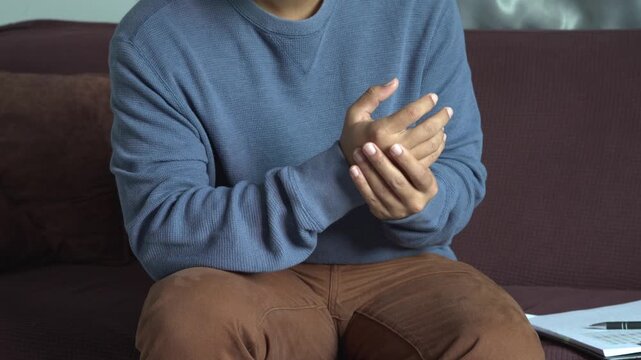 Young businessman feels numbness and severe pain in his wrist, arm, neck and shoulder, caused by sitting and working for a long time, massaging his sore hand with other hand, office syndrome concept.