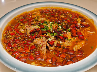 fresh slices of pork meat in the red spicy soup with red peppers in the plate