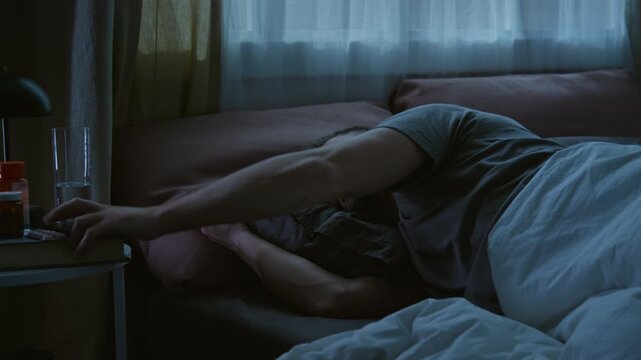 Time lapse of restless young Caucasian man lying in bed at night, taking sleeping medication, repeatedly checking smartphone, typing messages on social media and browsing internet
