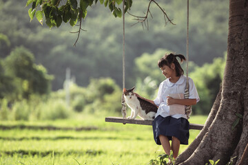 Girl in School Uniform Sitting on Swing Under Tree with Cat in Serene Green Field, Connecting with Nature and Animals in Peaceful Rural Landscape