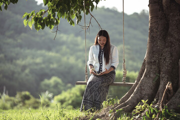A Young Woman Enjoys a Relaxing Moment on a Swing Beneath a Large Tree in a Lush Green Landscape Surrounded by Beautiful Nature