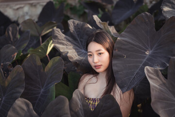 Woman in Nature Surrounded by Large Dark Green Leaves with Soft Natural Light and an Expression of...