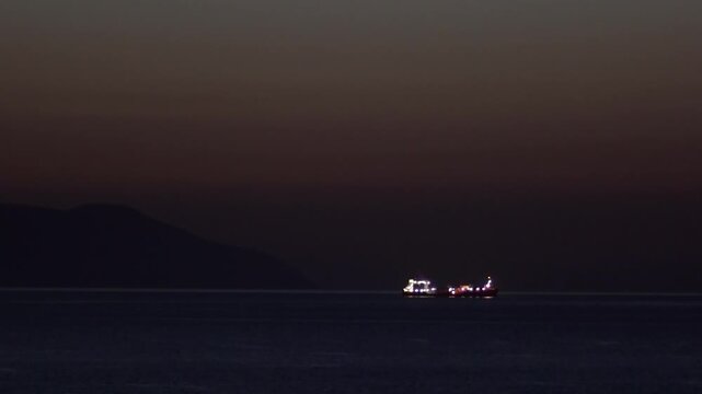 Seascape featuring a brightly lit vessel sailing under the deepening twilight