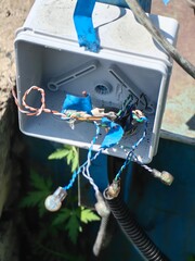Exposed electrical junction box showing open wires and potential hazards outdoors.