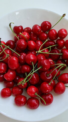 Fresh red cherries with stems on white plate close-up