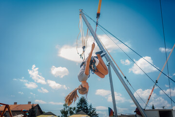 Girl jumping upside down on bungee trampoline under blue sky