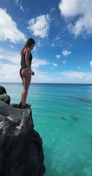 Young woman high jumping from volcanic rock overlooking vibrant blue Pacific ocean waters on Hawaii island