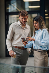 Business partners using smartphone and drinking coffee outdoors
