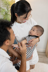 Obraz premium A man and a woman are sitting on a couch with a baby in between them. The baby is wearing a striped outfit. Scene is warm and loving, as the family is spending quality time together 