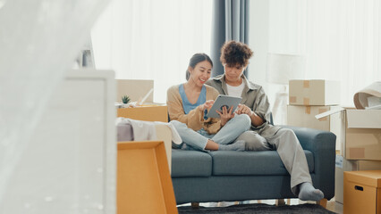 Young happy Asia couple sit on sofa couch use digital tablet online shopping furniture from...