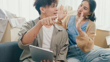 Young happy Asia couple sit on sofa couch use digital tablet online shopping furniture from...