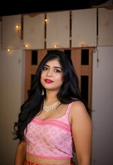 Fototapeta premium Portrait of a woman with long black hair wearing a pink top and a necklace indoors posing