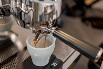 Close-up of espresso machine brewing coffee into a white cup on a digital scale, showing dual...