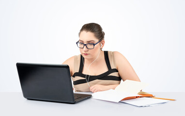 A focused woman, studying at a desk with a laptop and an open book, listens to music with...