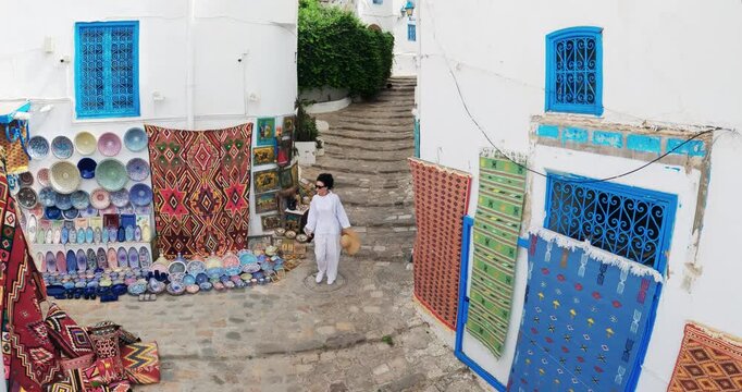 Sidi bou Said, Tunisia - Jan 11, 2025: Stylish tourist woman Exploring Sidi Bou Said Charming Streets and Artisan Market, aerial view