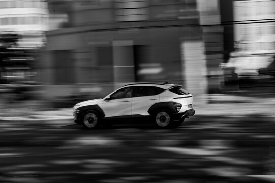 Fototapeta White SUV driving on urban street with motion blur, black and white transportation photography