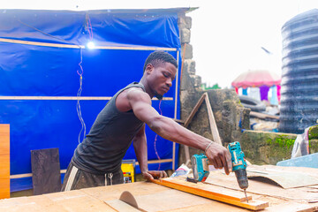 Young African carpenter standing, cutting wooden board