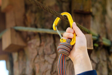 Closeup of child hand fastening yellow carabiner to safety rope at adventure park, secure...