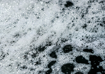 Obraz premium Close-up shot of white foam with bubbles against a dark background, creating a textured and abstract pattern.