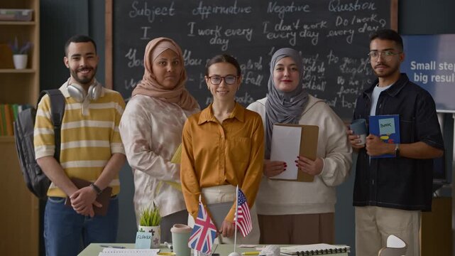 Medium portrait of Caucasian female teacher standing with multicultural students in front of blackboard in modern English classroom