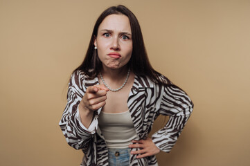 Woman expressing anger while pointing at the camera in a neutral-toned setting during daylight