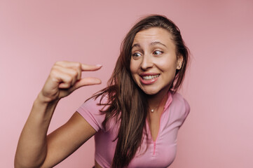 Woman playfully demonstrating a small size with hand gesture against a pink background while smiling