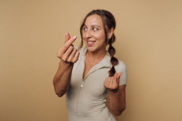 Smiling woman in form-fitting outfit making hand gesture against neutral background in a creative...